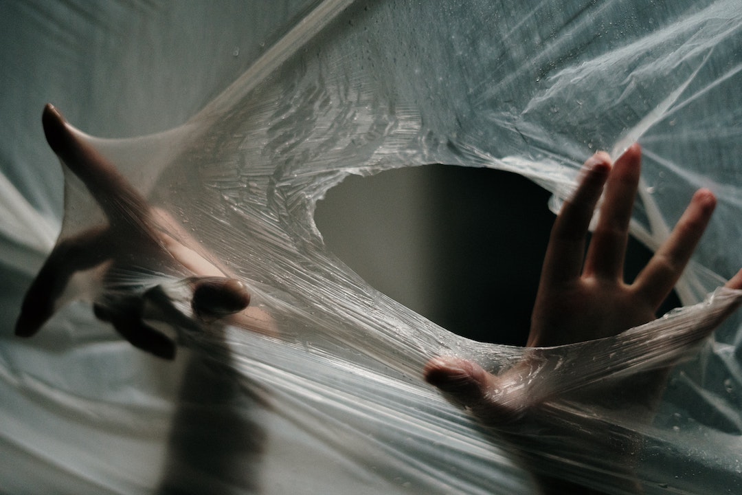 Pièges à spam - photo de mains passant par un trou dans une feuille de plastique transparent